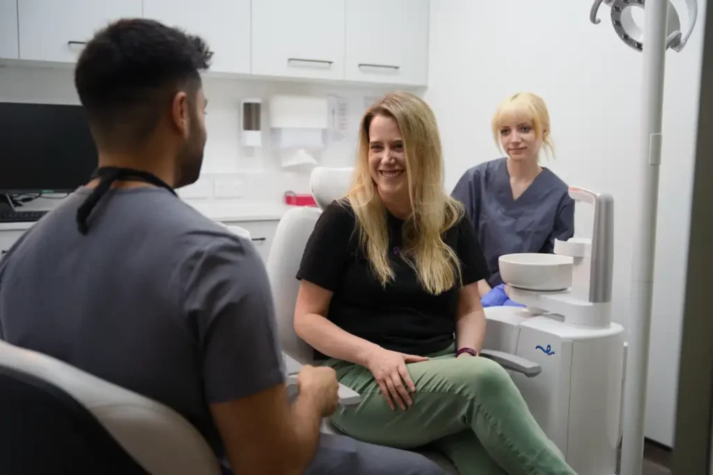 A smiling patient receiving a consultation for professional teeth whitening at Oradent Dental Care, featuring Boutique and Enlighten whitening kits on a clinical tray.